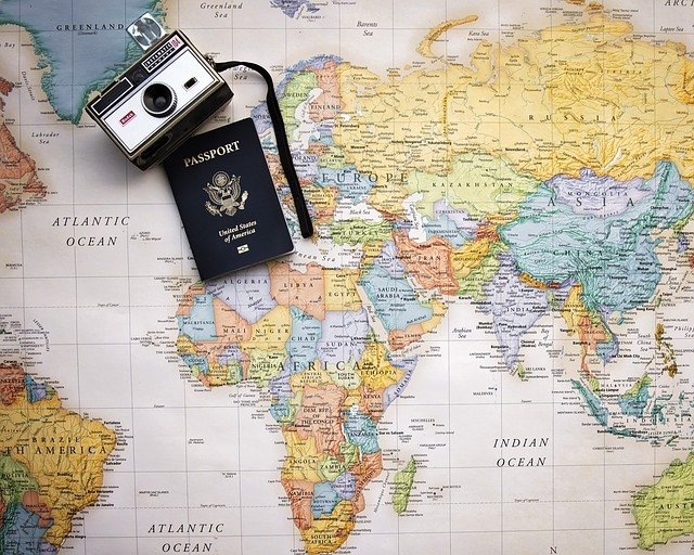 Alter Fotoapparat und amerikanischer Reisepass auf bunter Weltkarte liegend